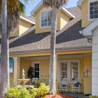 A charming yellow house with a welcoming front porch and palm trees in the garden.