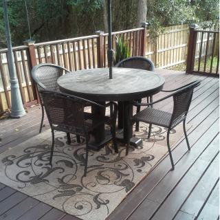 A patio with a round table, four chairs, and a decorative rug on a wooden deck.