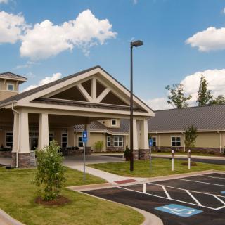 A modern building entrance with a covered driveway and adjacent parking lot under a partly cloudy sky.