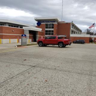 A red vehicle parked outside a modern brick building under a cloudy sky.