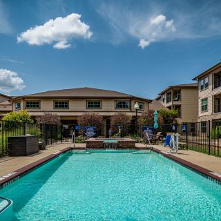 A sunny view of a swimming pool surrounded by apartment buildings under a clear blue sky.