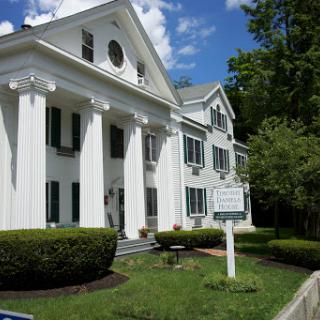 A classic white-columned building surrounded by lush landscaping under a partly cloudy sky.