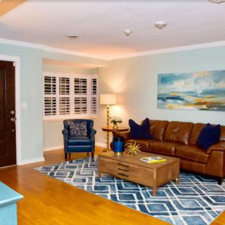 A cozy living room with a brown leather sofa, blue armchair, and decorative rug, featuring artwork on the wall.