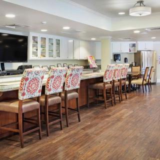 A modern kitchen with a large counter and colorful chairs, featuring wood flooring and contemporary lighting.