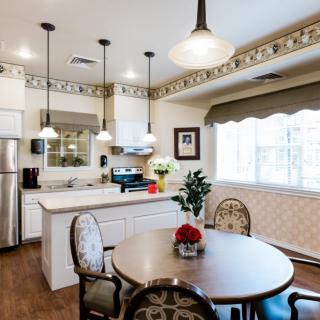 A modern kitchen and dining area featuring white cabinets, stainless steel appliances, and pendant lighting.