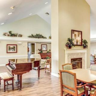 A spacious and well-decorated community room featuring a piano, seating areas, and a fireplace.