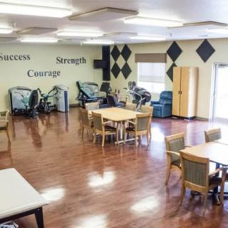 A bright exercise room featuring fitness equipment, tables, and motivational words on the walls.