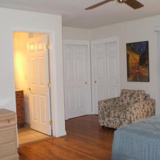 A cozy bedroom with a bed, patterned chair, closet doors, and a piece of artwork on the wall.