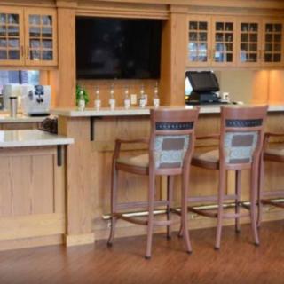 A cozy bar area with wooden cabinets and stools, featuring a flat-screen television and a variety of bottles displayed on the counter.
