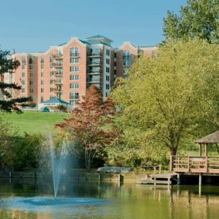 A scenic view of a building near a pond with a fountain, surrounded by trees and natural beauty.