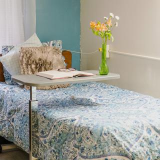 A hospital room with a bed, a tray table holding flowers and an open book.