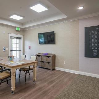 A well-lit conference room with a wooden table, chairs, and a TV screen on the wall.