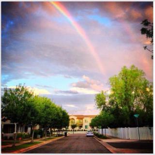 A beautiful rainbow arches over a peaceful neighborhood street at sunset.
