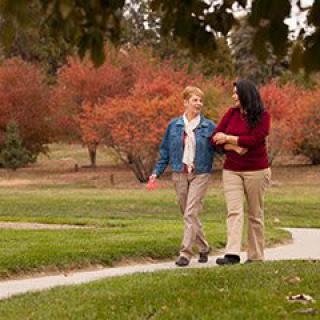 Two people walking arm in arm along a pathway in a park with autumn foliage.