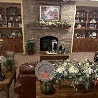 A cozy living room featuring a decorative fireplace, shelves filled with items, and elegant floral arrangements.