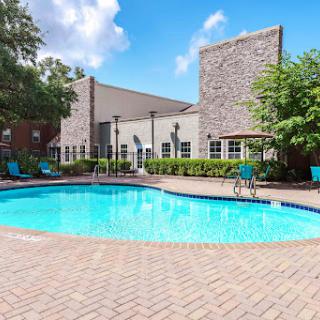 A serene outdoor pool area surrounded by lush greenery and a clear blue sky.