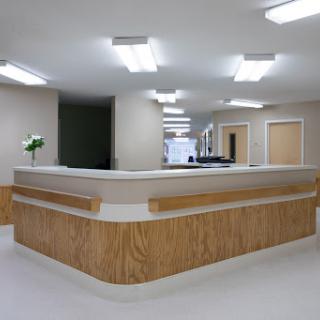 A modern reception area in a healthcare facility, featuring a wooden front desk and bright overhead lighting.