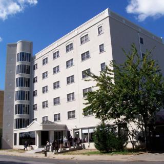 A modern hospital building with a cylindrical glass stairwell and surrounding trees.