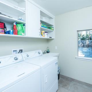 A bright laundry room featuring a washing machine, dryer, and shelves stocked with detergent.