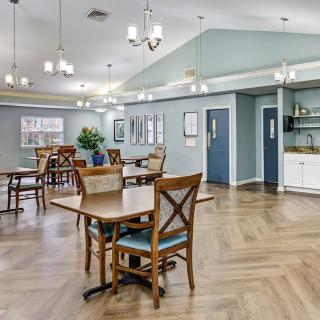 A spacious dining area with wooden flooring, featuring several tables and chairs under bright chandeliers.