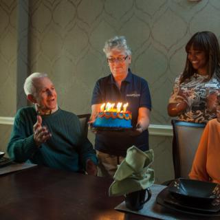 A group of people celebrating a birthday with a cake and lit candles.