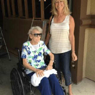 A woman stands beside an elderly person in a wheelchair.