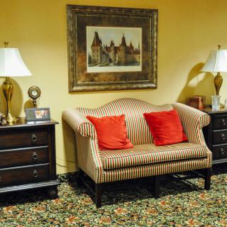 A vintage styled living area featuring a striped sofa with red cushions, flanked by two dark wooden side tables and lamps, set against a backdrop of warm yellow walls adorned with artwork.