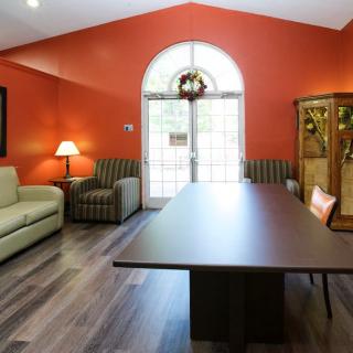 A well-lit living or meeting room with orange-painted walls, featuring a large table, sofas, and chairs.