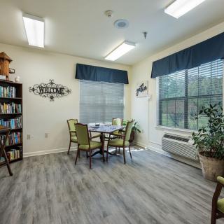 A cozy reading room with a table and chairs, bookshelves, and large windows.