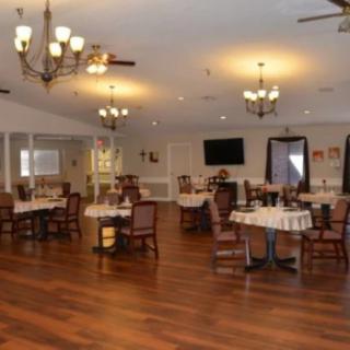 A spacious dining area with wooden floors, elegantly set tables, and chandeliers hanging from the ceiling.