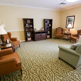 A cozy living room with a mix of comfortable chairs and a sofa, featuring decorative shelves and a patterned carpet.