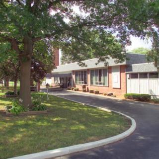 A residential brick house with a curved driveway surrounded by trees.