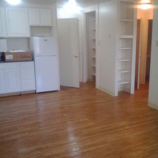 A minimalist apartment kitchen with wooden floors and white cabinetry.