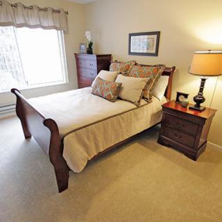 A cozy bedroom with a wooden bed and matching nightstand, softly lit by a table lamp.