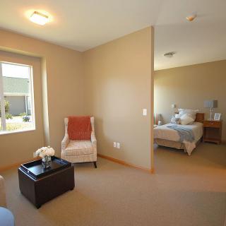 A cozy interior view featuring a small living area with a chair and ottoman, adjacent to a bedroom with a neatly made bed.