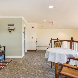 A cozy interior space with a dining area featuring tables and chairs, carpet flooring, and a railing.