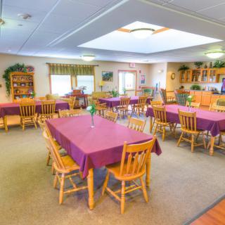 A cozy dining room with tables covered in purple tablecloths and wooden chairs.