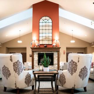 A cozy living room with elegant armchairs facing a brick fireplace, complemented by modern decor and a large window above.