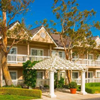 A charming two-story house with a white pergola and surrounded by trees under a clear blue sky.