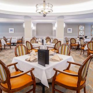An elegant dining area with neatly arranged tables and chairs, featuring a central chandelier.