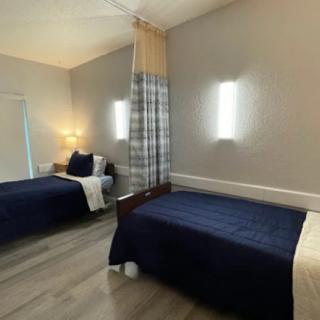 A modern bedroom with two beds, separated by a curtain, featuring sleek lighting and contemporary decor.