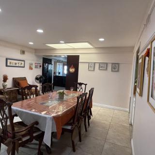 A spacious dining room featuring a large table with chairs, adorned with artwork on the walls and well-lit by ceiling lights.