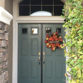 A front door decorated with an autumn wreath and surrounded by greenery.