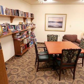 A cozy library room with bookshelves, a table with chairs, and a sofa.