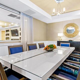 A modern and elegant dining room featuring a reflective table, stylish chairs, a decorative mirror, and a chandelier.