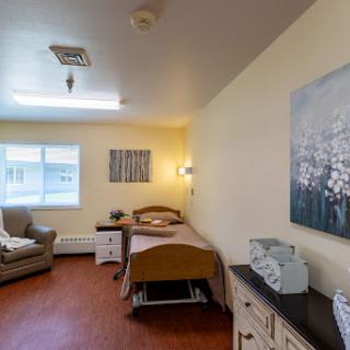 A well-lit hospital patient room featuring a bed, a cozy sofa, and decorative artwork.