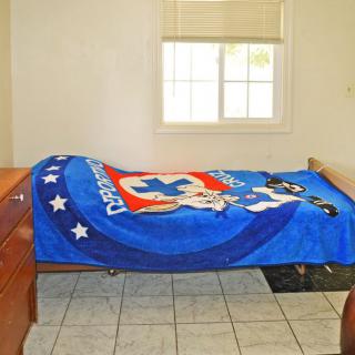 A simple bedroom with a bed covered by a blue blanket featuring cartoon characters.