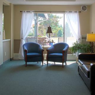 A cozy living room with two blue chairs, a large window with curtains, and a lamp beside a sofa.