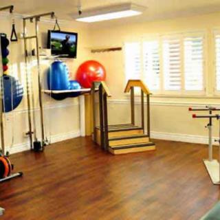 A rehabilitation room equipped with various exercise and therapy tools, including exercise balls, parallel bars, and a small staircase apparatus.