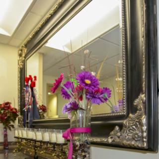 A decorative interior scene with a large ornate mirror, colorful flowers in a vase, and candles.